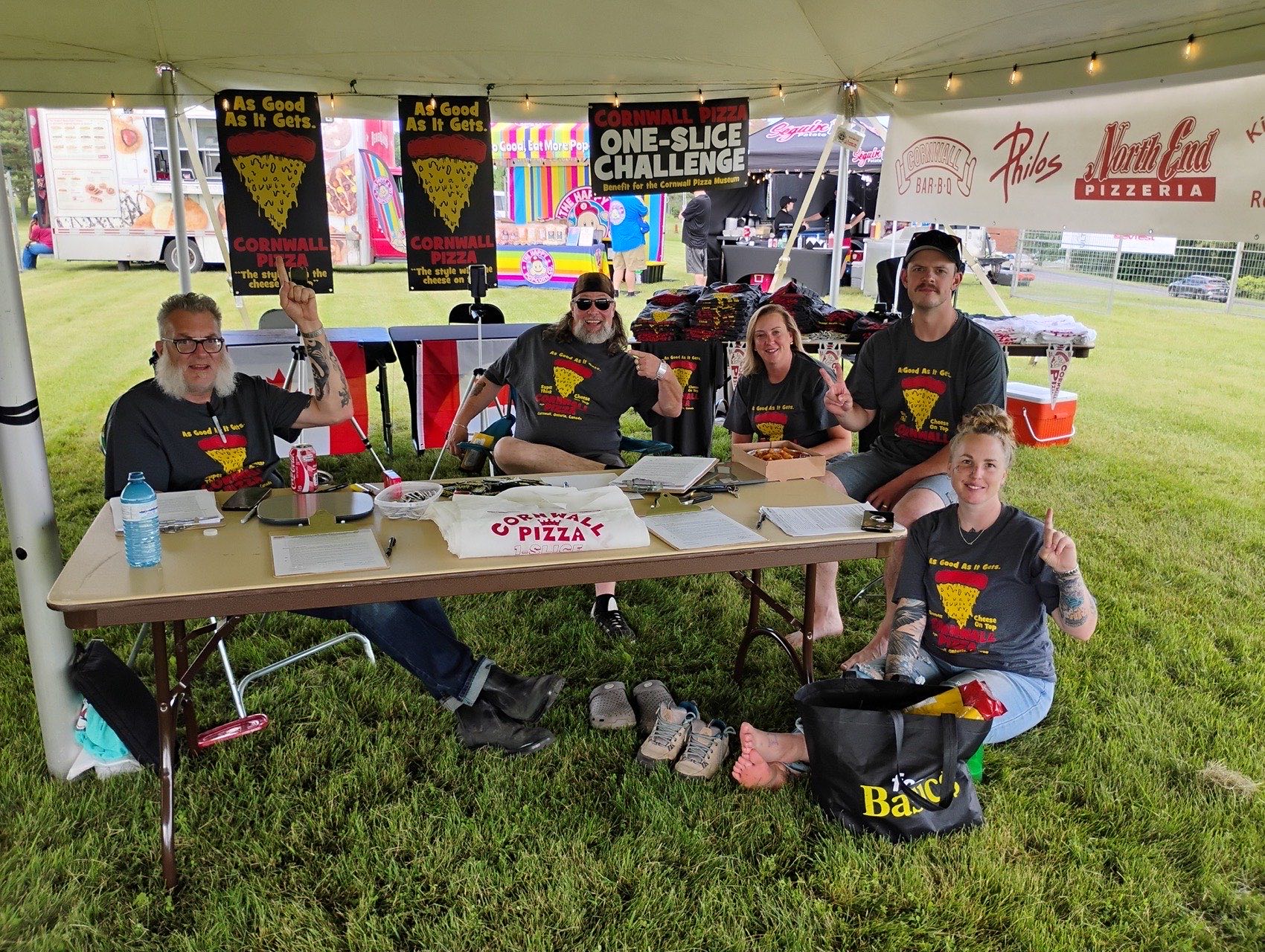 The Cornwall Pizza One-Slice Challenge crew under their tent at DevFest, with hand-painted banners and Cornwall Pizza T-shirts.