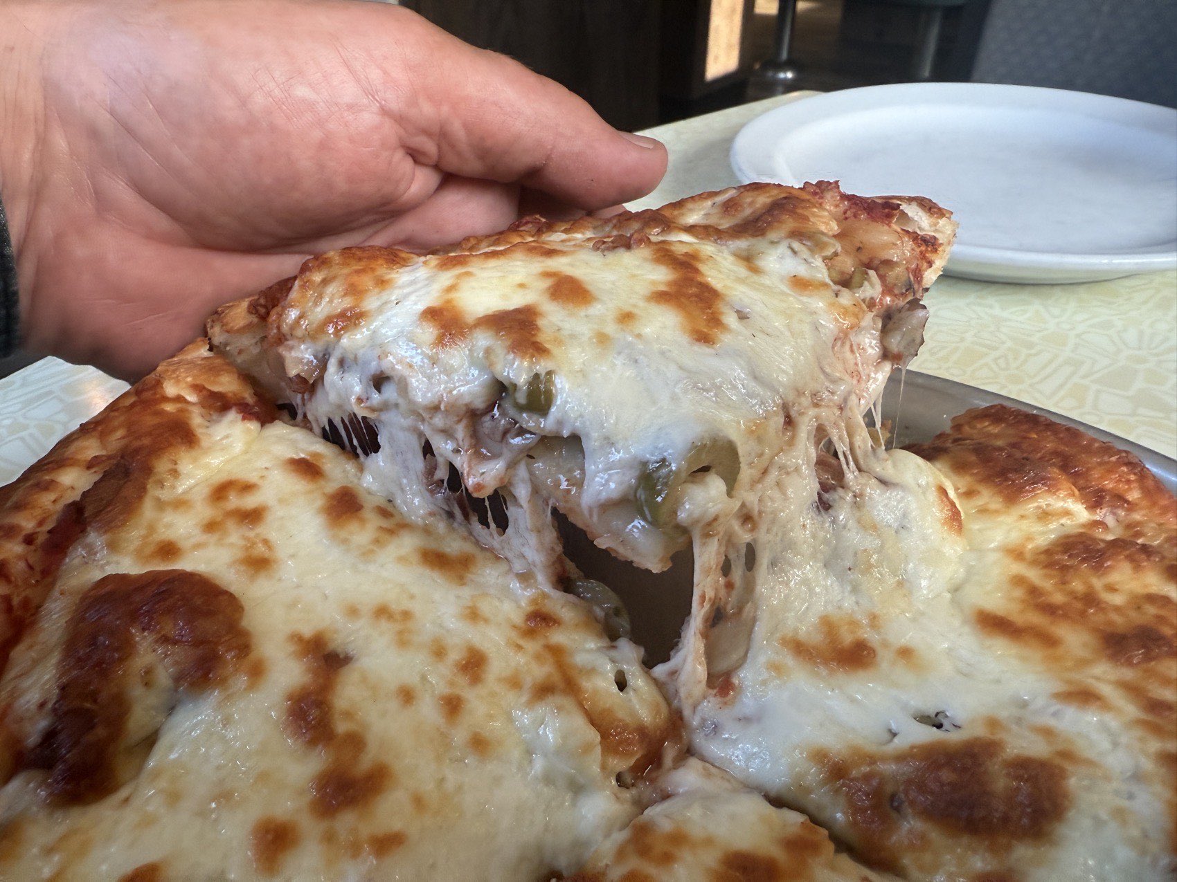 A slice of thick Cornwall pizza being lifted from the pan, cheese stretching in long strands.